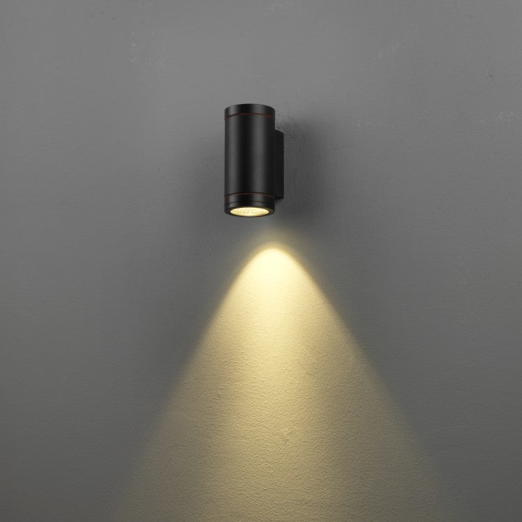 Black outdoor wall light fixture on a gray wall with a soft glow.