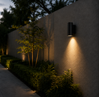Outdoor wall light fixture on a concrete wall with plants and trees in the background.